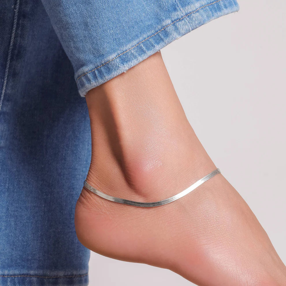 Silver anklet on a person's ankle with a denim background